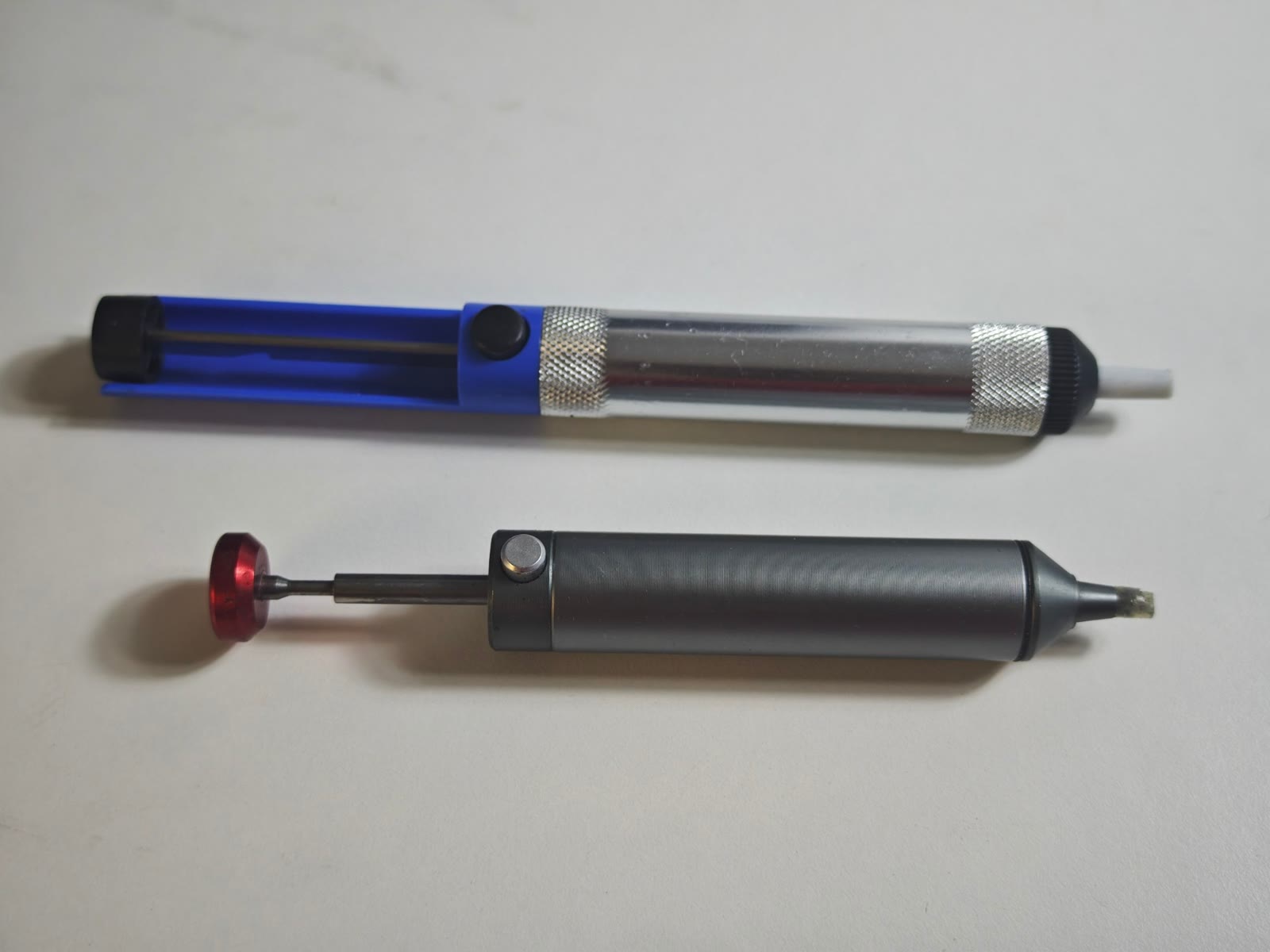 Dos bombas de succión desoldadoras (desoldadores de émbolo), una azul y otra gris con gatillo rojo